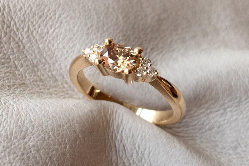 Guldring med oval champagnefarvet diamant og hvide brillianter på siden.